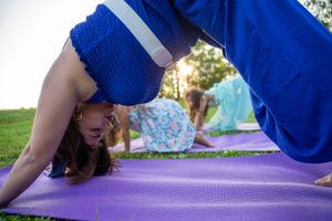 Person performing stretching exercises on a blue yoga mat in a park setting.