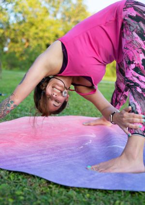 Yoga practitioner demonstrating flexibility pose on tie-dye mat in outdoor setting.