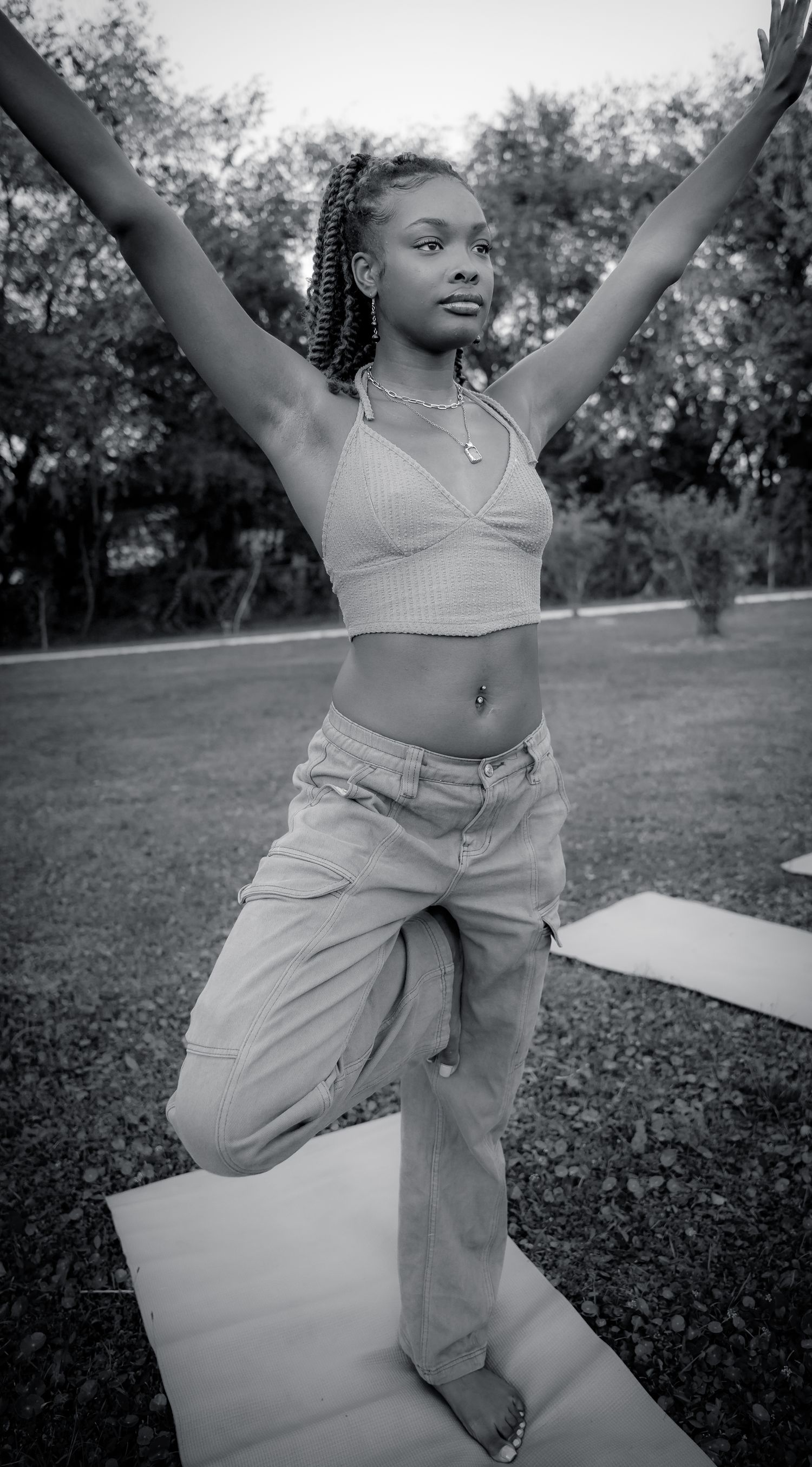 Black and white photo of a person in a crop top and jeans striking a yoga pose outdoors.