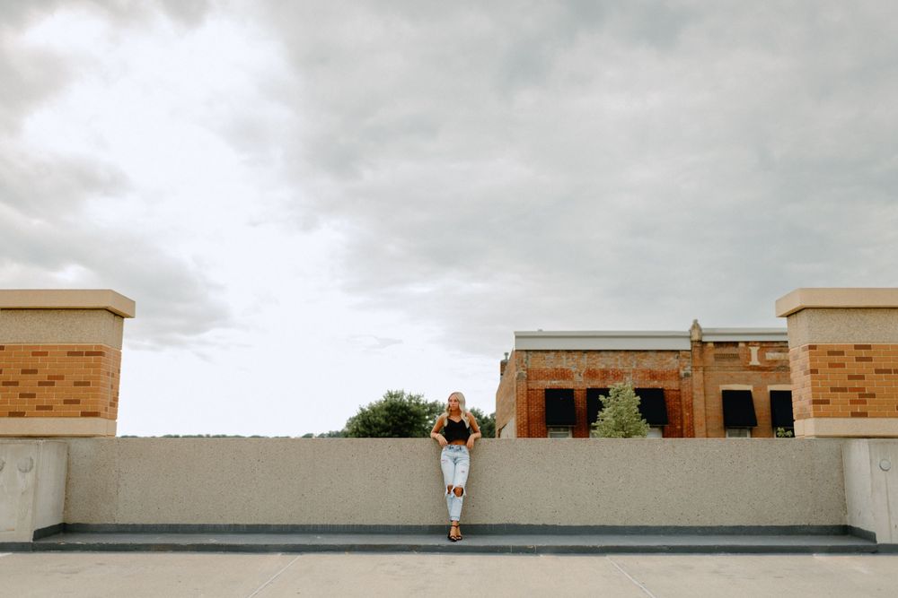 A person standing alone on a rooftop against a cloudy sky between two brick pillars.
