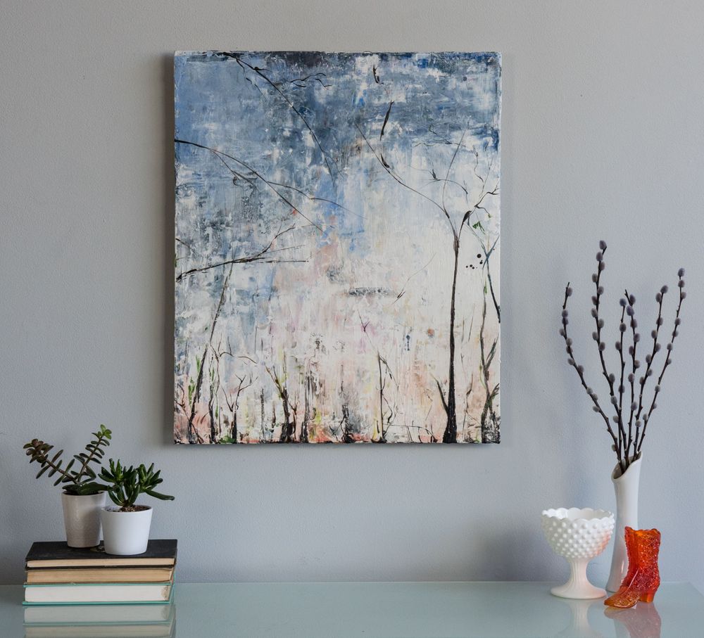 Abstract winter landscape artwork displayed on a gray wall with decorative accessories on a floating shelf.