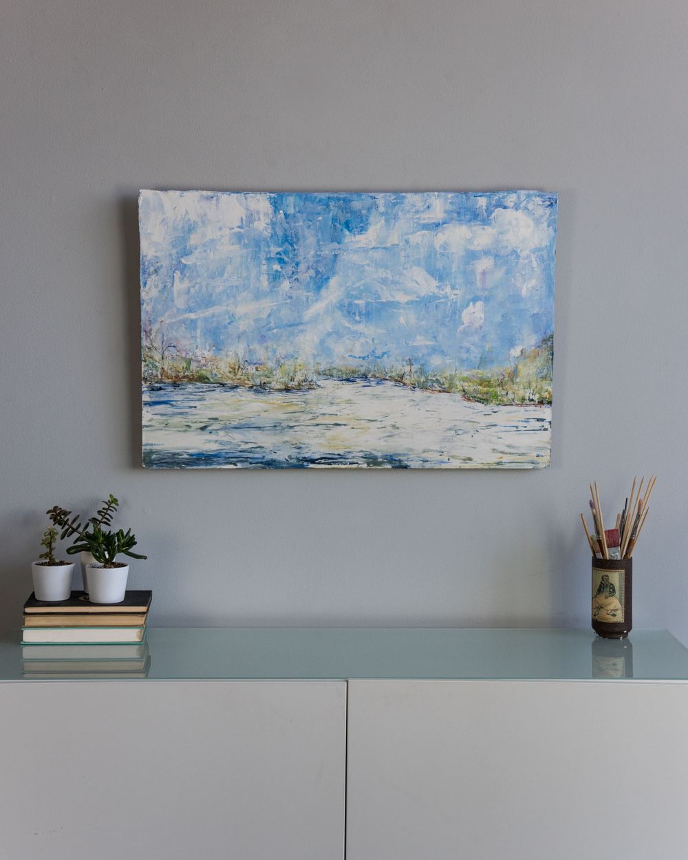 Serene blue and white landscape painting mounted above white furniture with minimal decor.