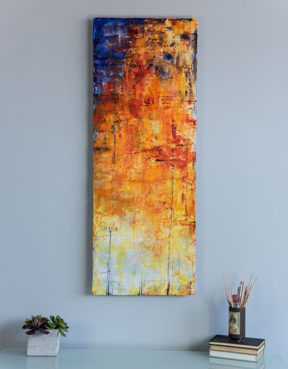 Vibrant orange and yellow abstract painting displayed on light gray wall with shelf accessories.