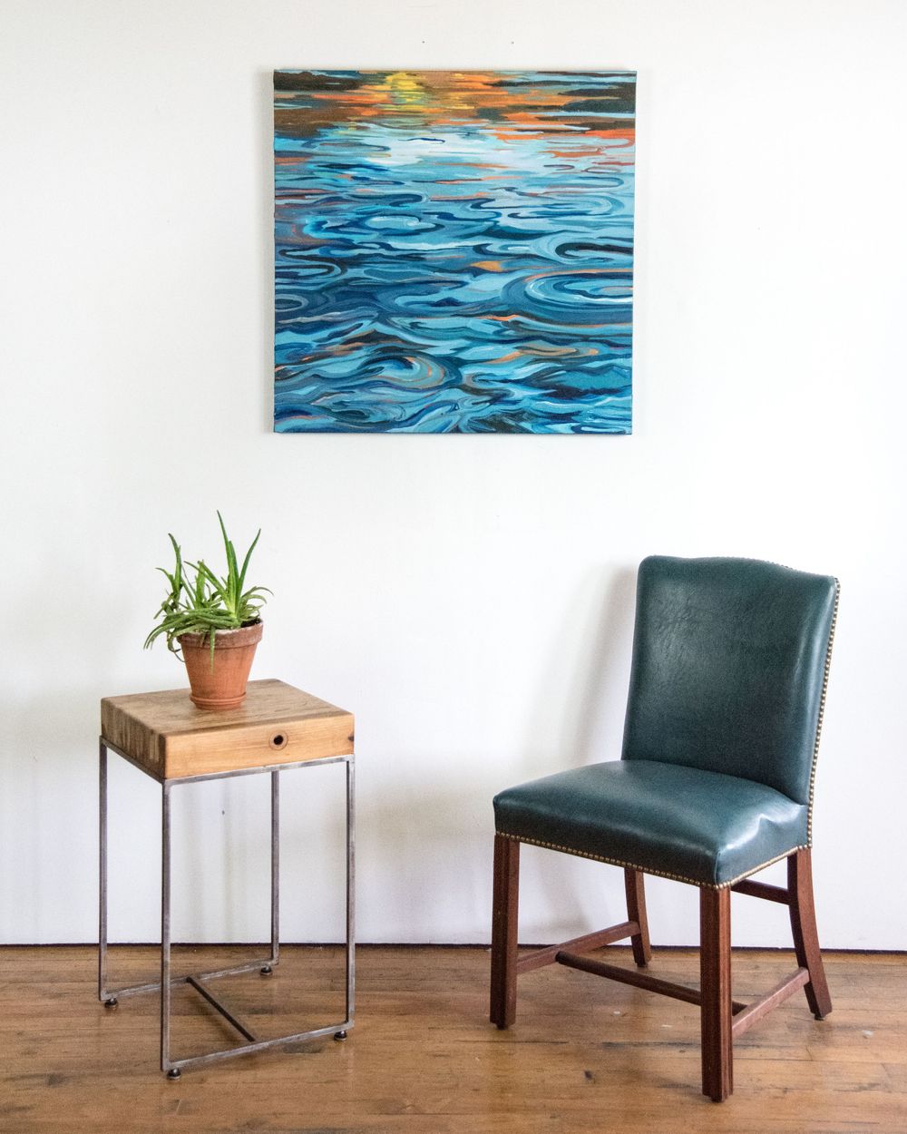 Ocean wave painting mounted above modern furniture with teal upholstery and wooden accents.