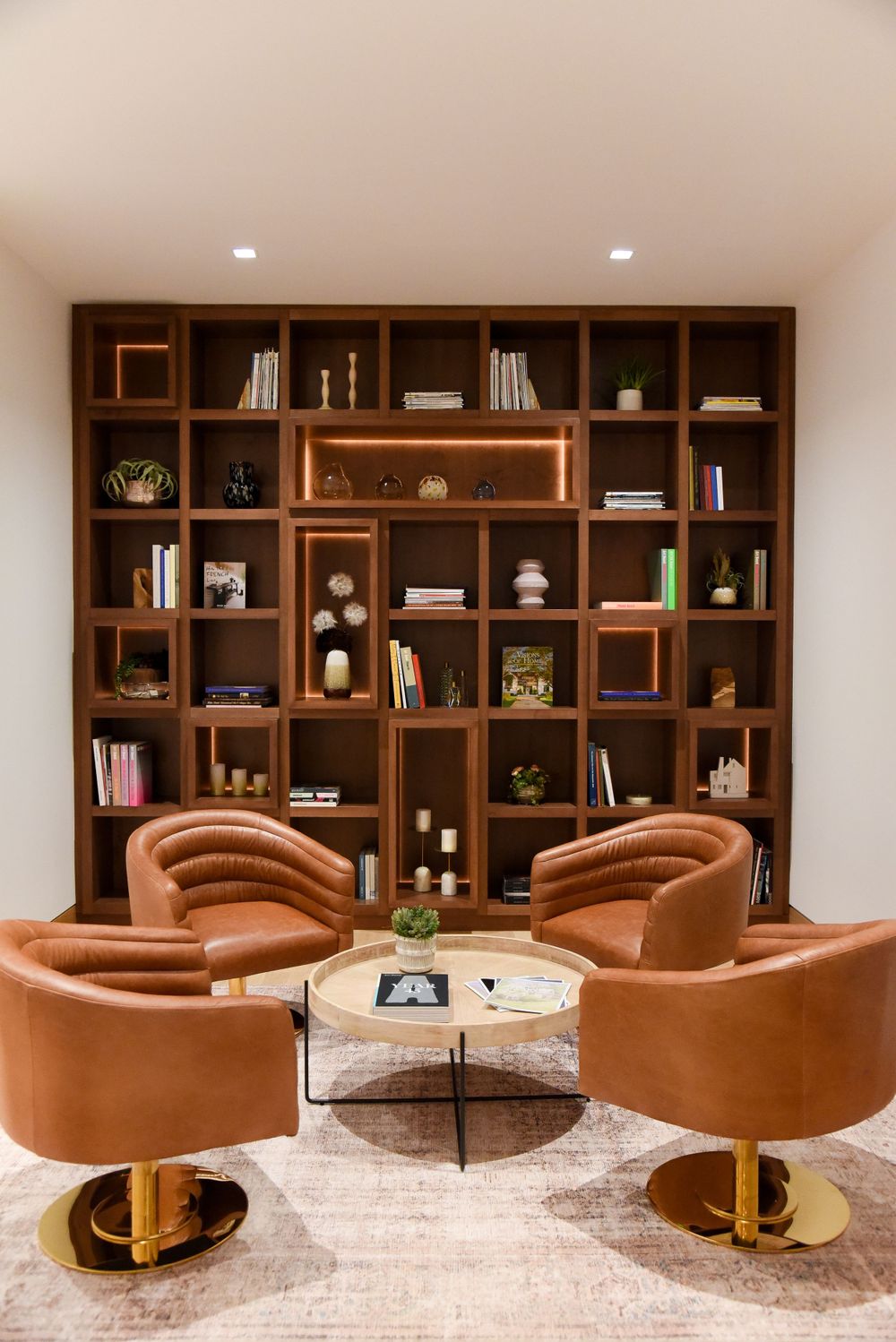 Stylish reading nook with brown leather swivel chairs and built-in wooden bookshelf wall.