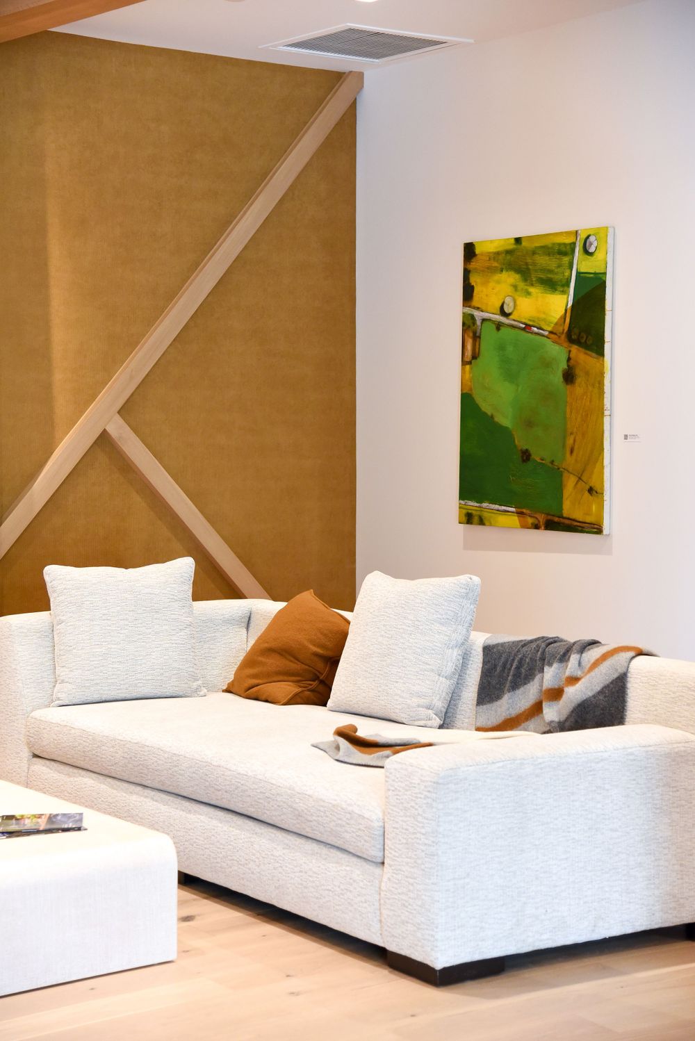Modern living room with white sectional sofa and abstract green artwork against brown accent wall.