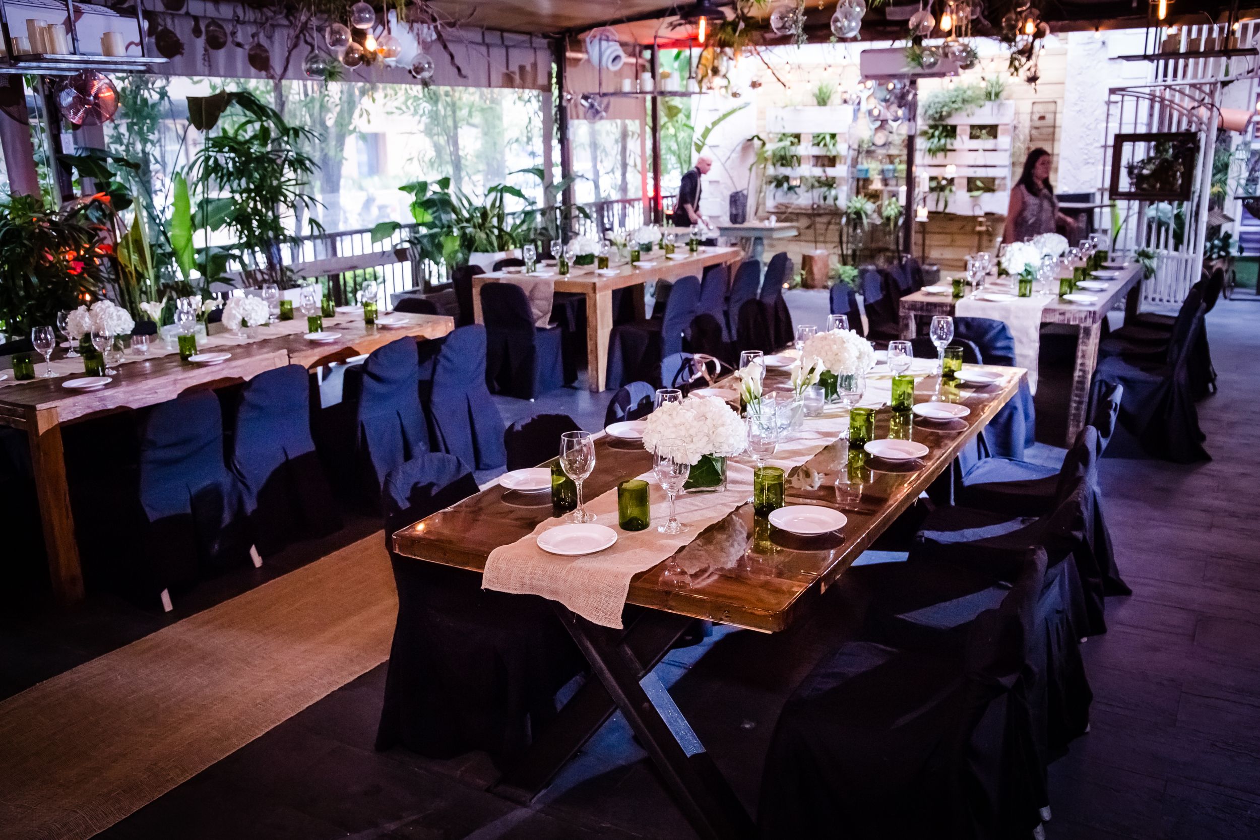 Wedding reception venue with long tables set for dining under warm lighting.