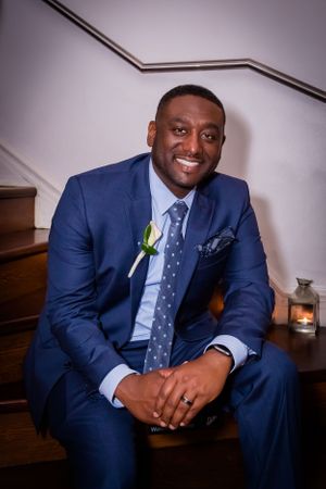 A groom in a navy blue suit poses for formal wedding portraits in an elegant setting.
