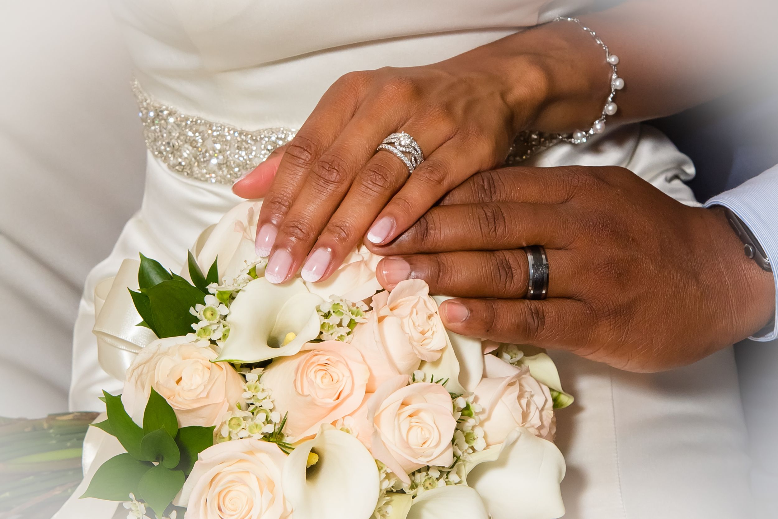 Close-up details of wedding rings and a white floral bouquet with roses and lilies.