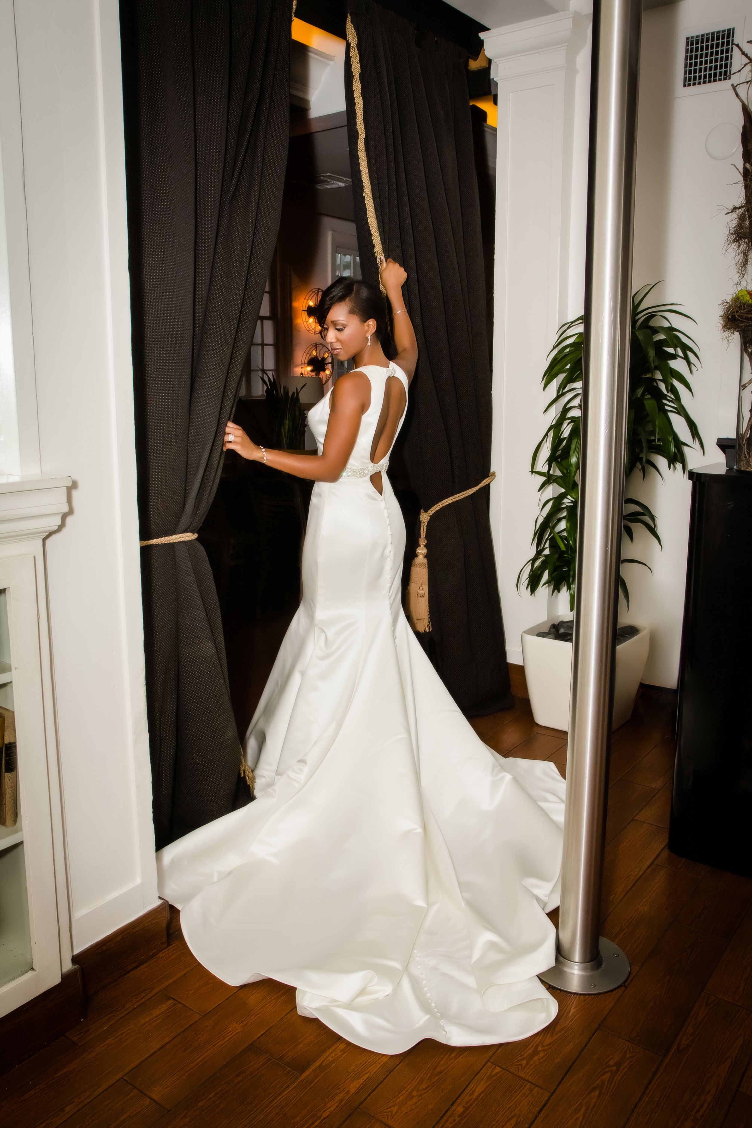 Bride in flowing white gown poses gracefully against dark curtained backdrop.