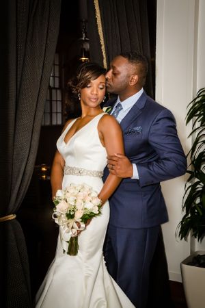 A couple shares an intimate moment in formal wedding attire against a dark backdrop.