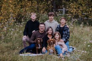 Family sits in tall grass with their two dogs during autumn.