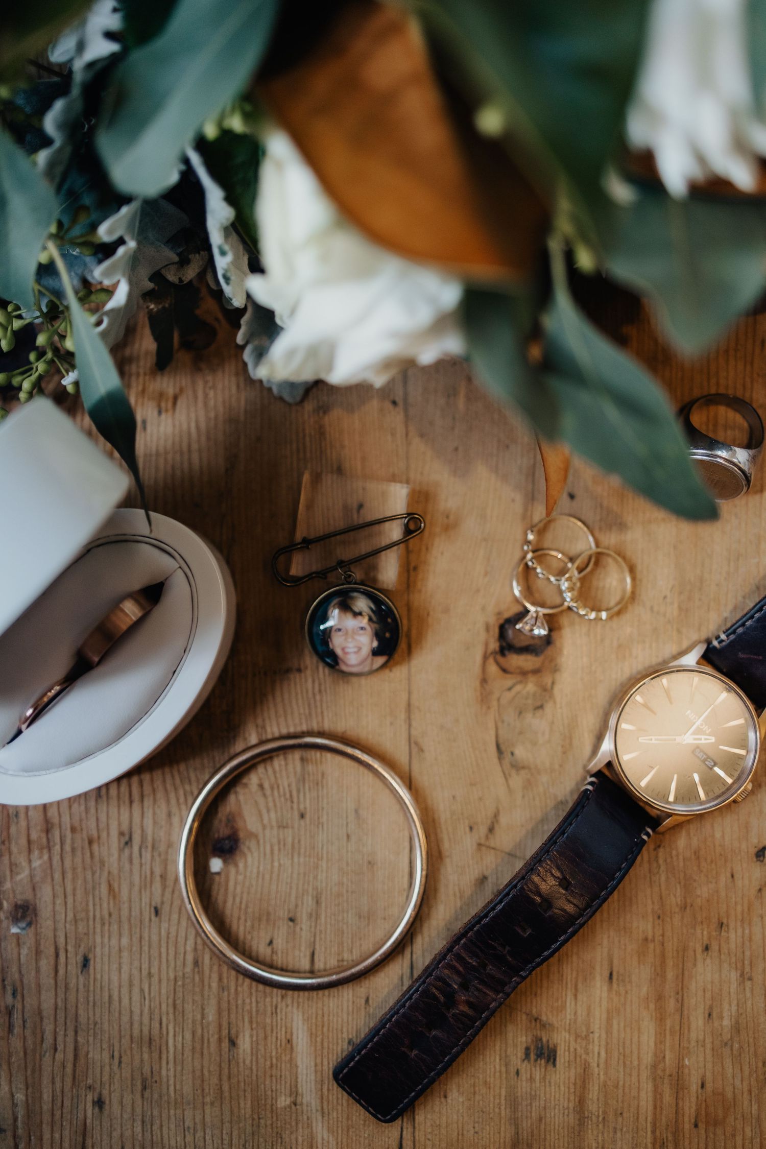 Wedding accessories including watch, rings and jewelry arranged on wooden surface.