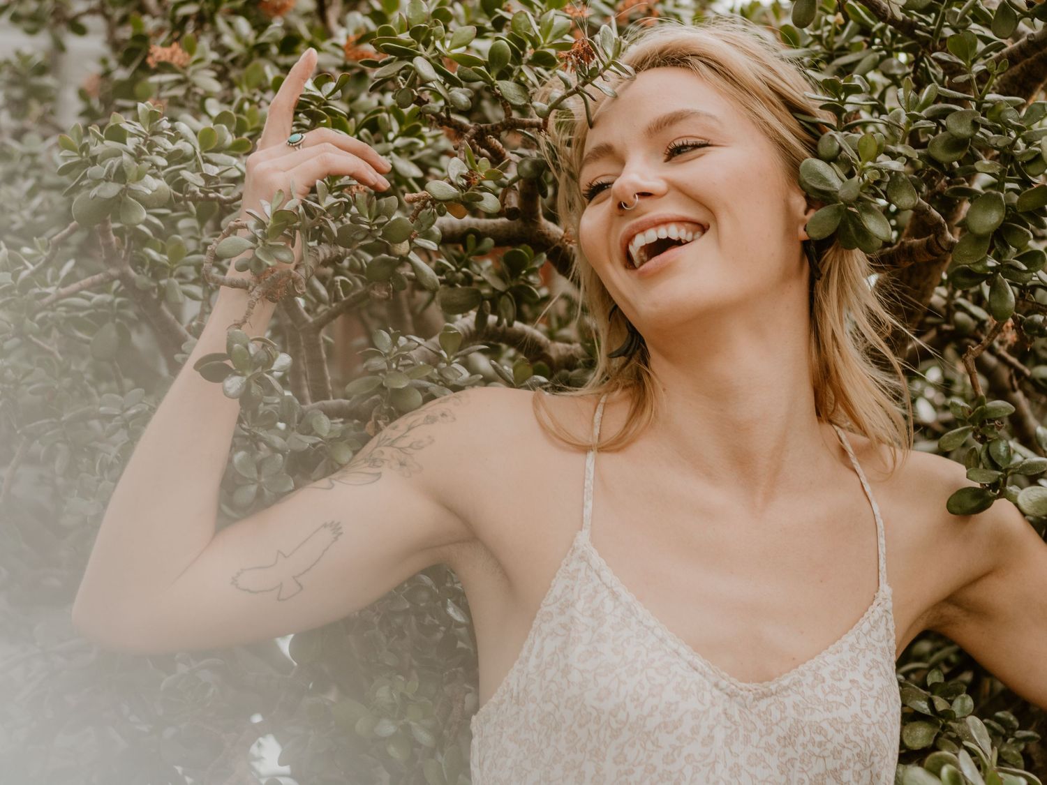 Joyful summer portrait surrounded by green leaves and natural sunlight.