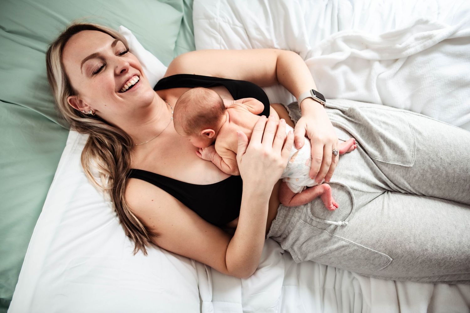 Woman laying in bed smiling. She is holding her newborn baby to her chest.