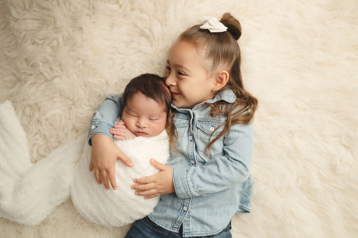 Sweet sibling portrait with older child cuddling newborn baby on ivory background.