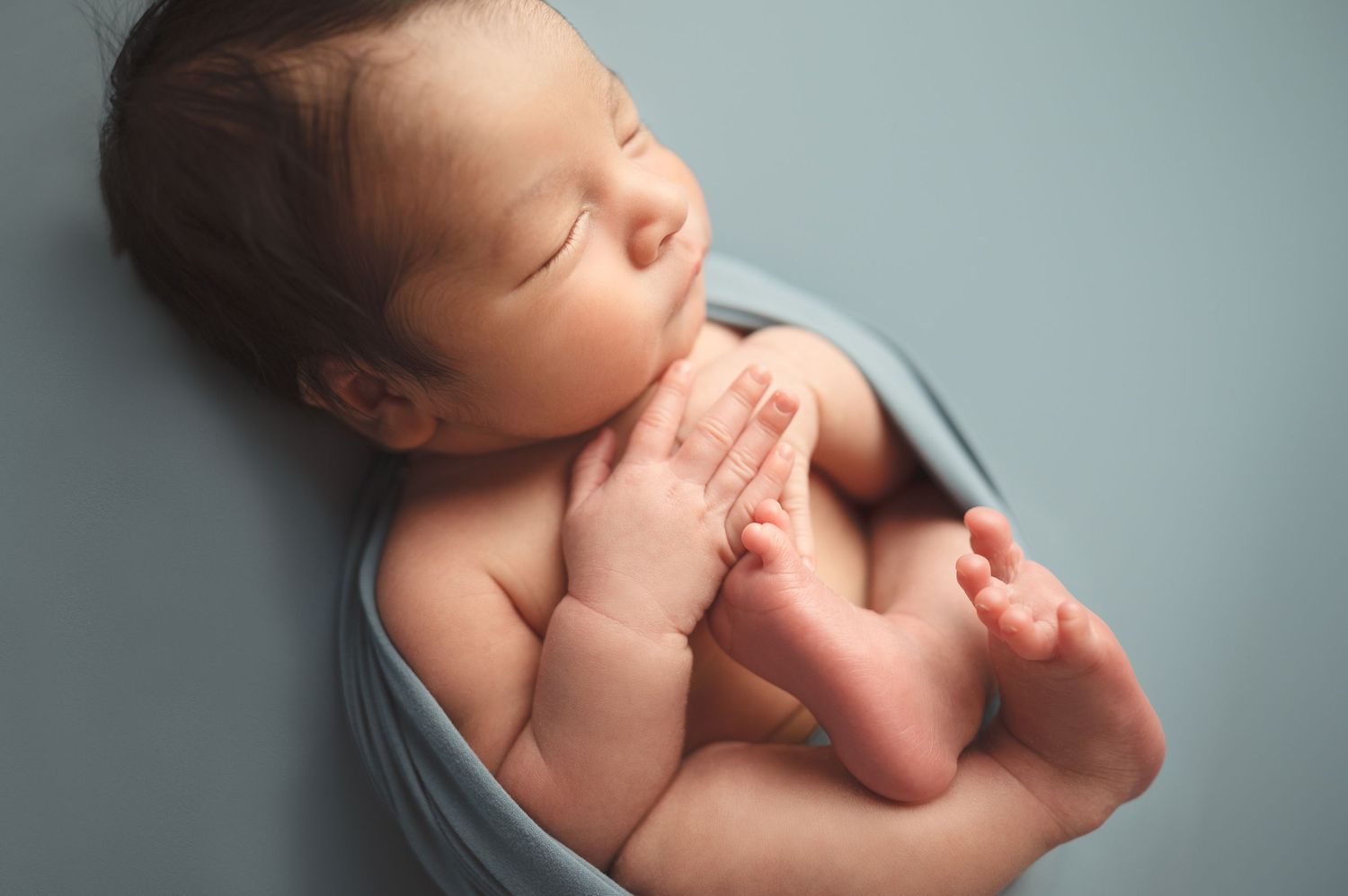 Sleeping newborn in light blue wrap photographed from various angles.