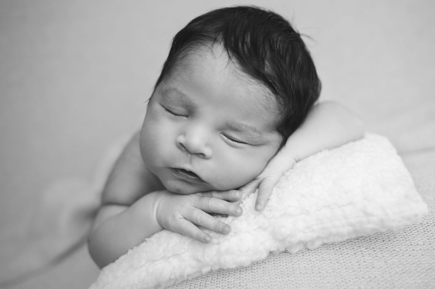 Black and white portraits of sleeping newborn on soft white bedding.
