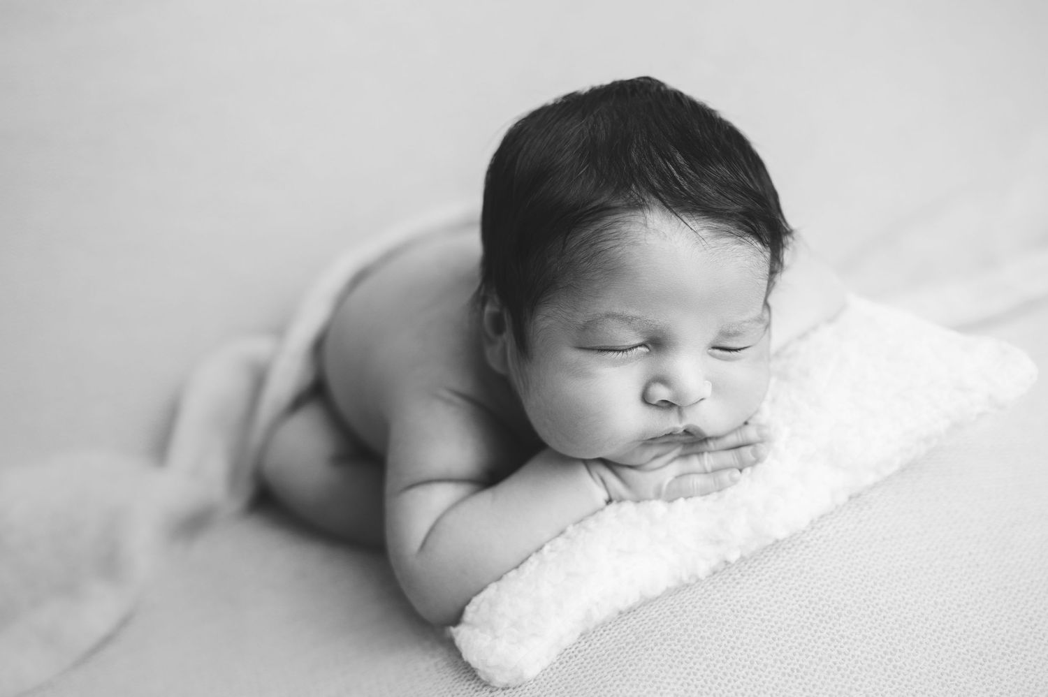 Artistic black and white series showing peaceful sleeping newborn on white backdrop.