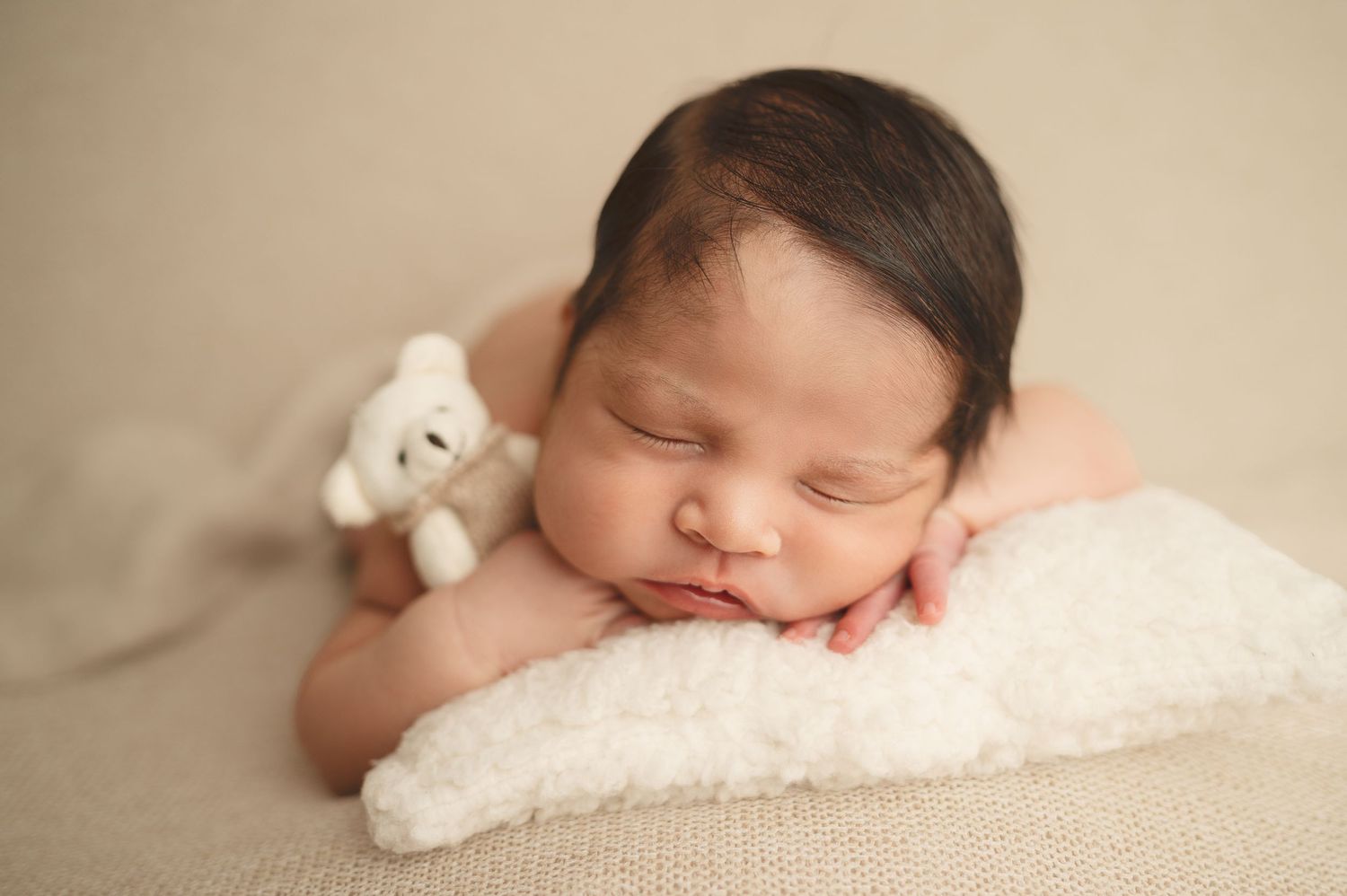 Sleeping newborn photographed on beige backdrop with small plush toy.