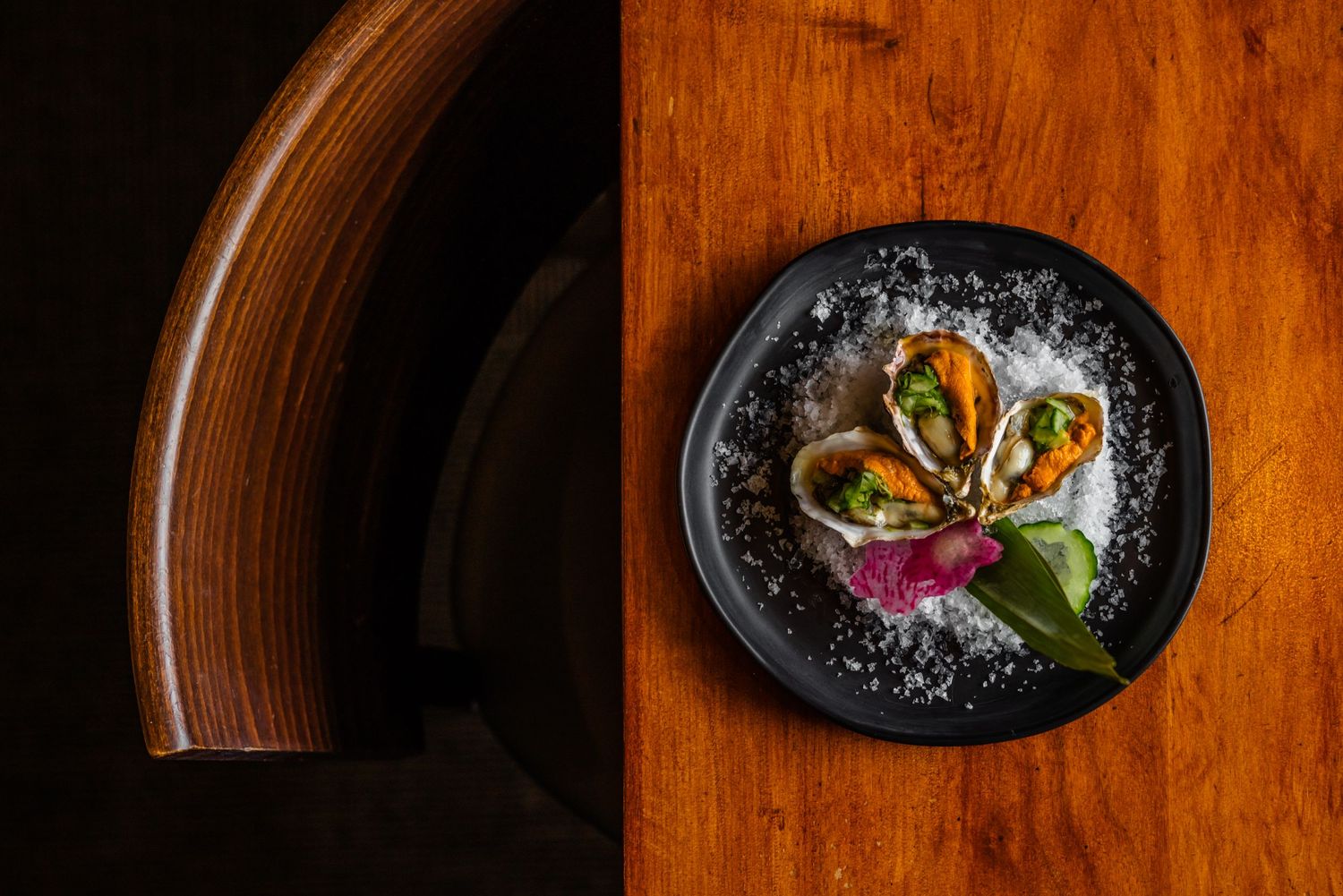Elegant seafood dish presented on black plate with crushed ice and garnished with fresh herbs.
