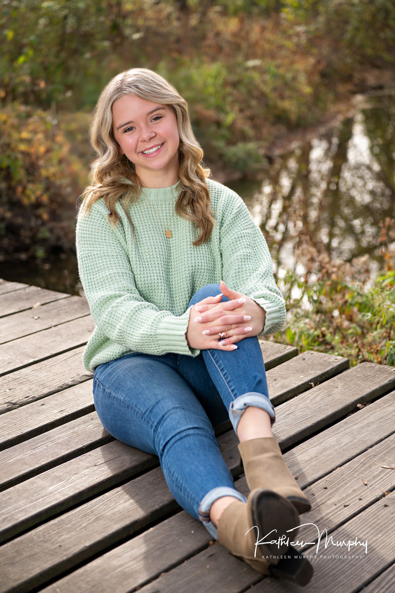 Person in mint sweater and jeans sitting casually on wooden deck.