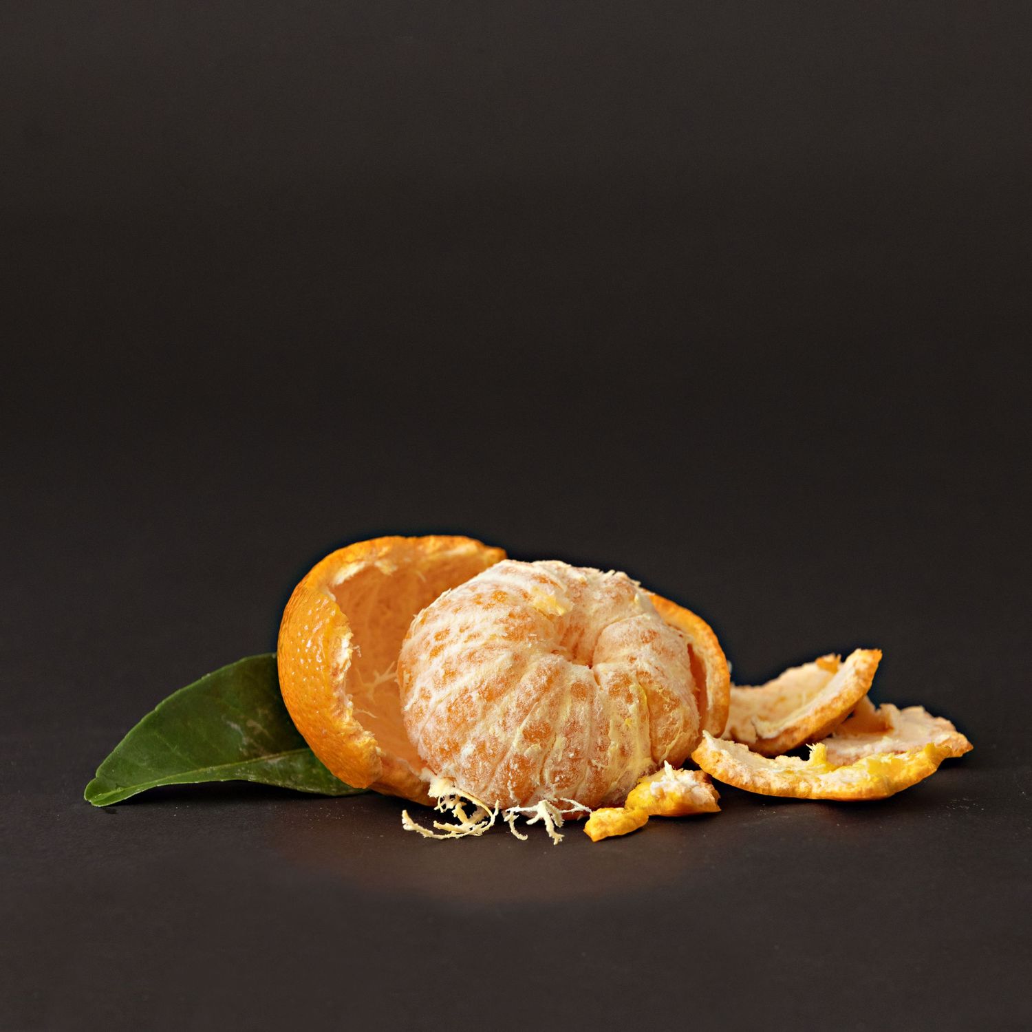 Peeled mandarin orange with segments and peel on a dark surface.