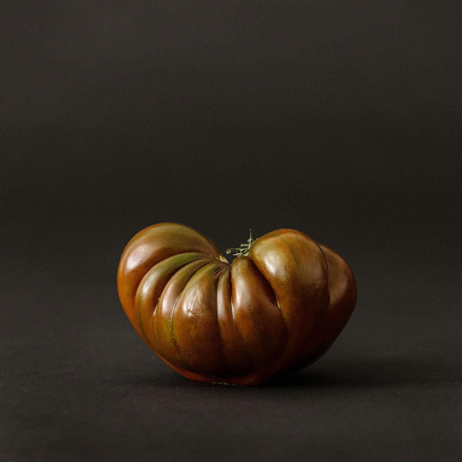 Large heirloom tomato with deep ridges photographed against dark background.