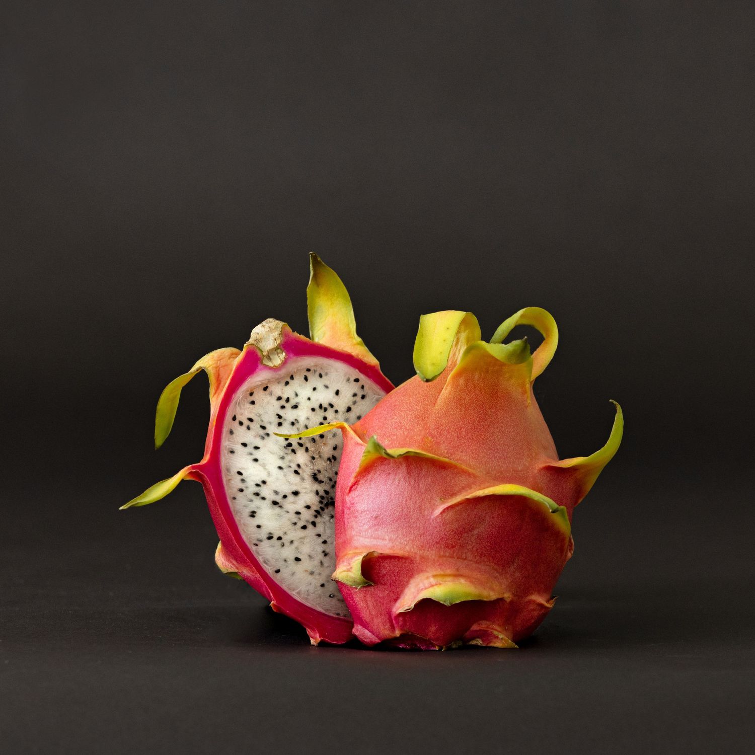 Halved dragon fruit with vibrant pink skin and speckled white flesh.