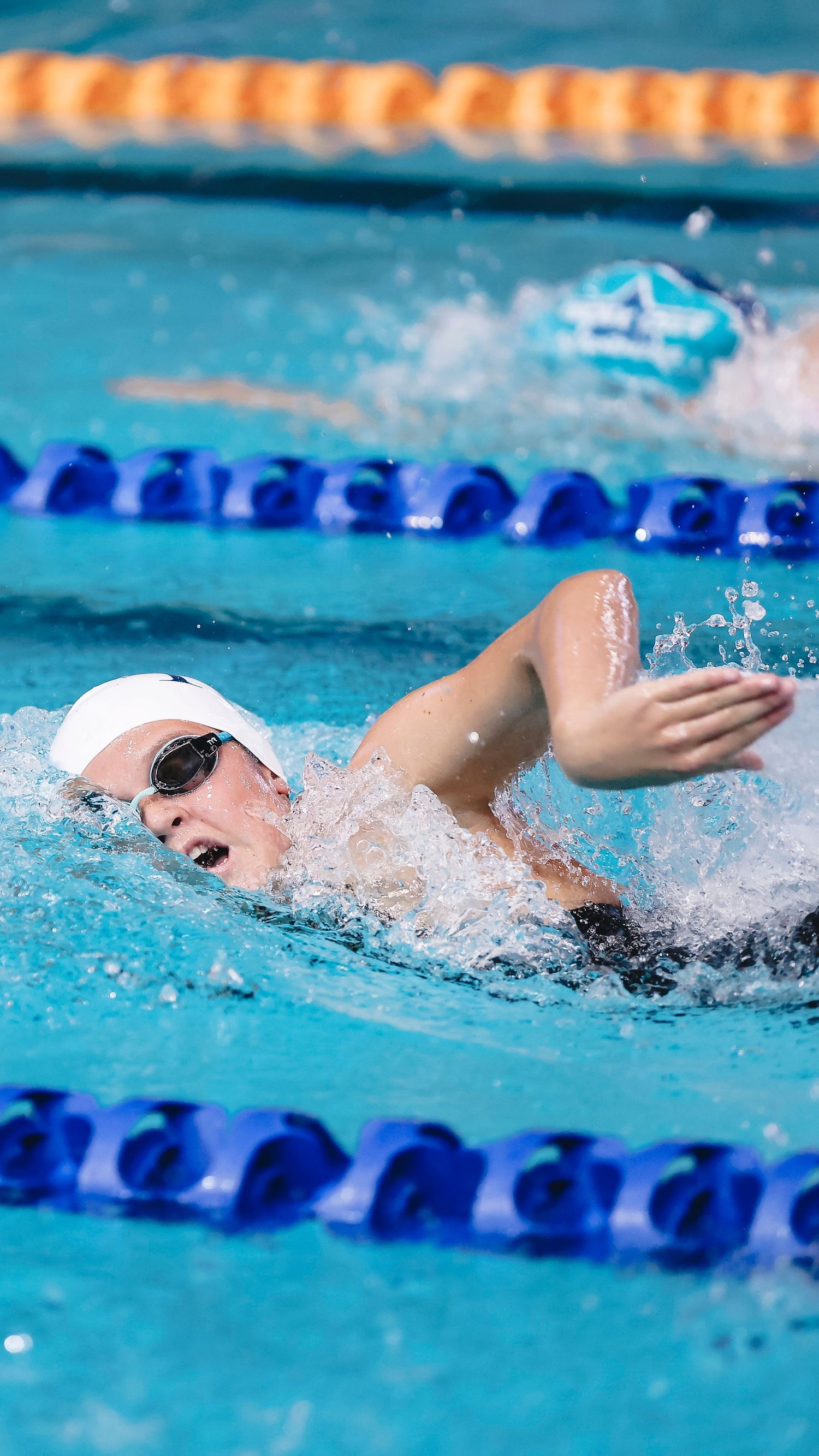 Competitive swimmer performing freestyle stroke in blue pool lane during race.