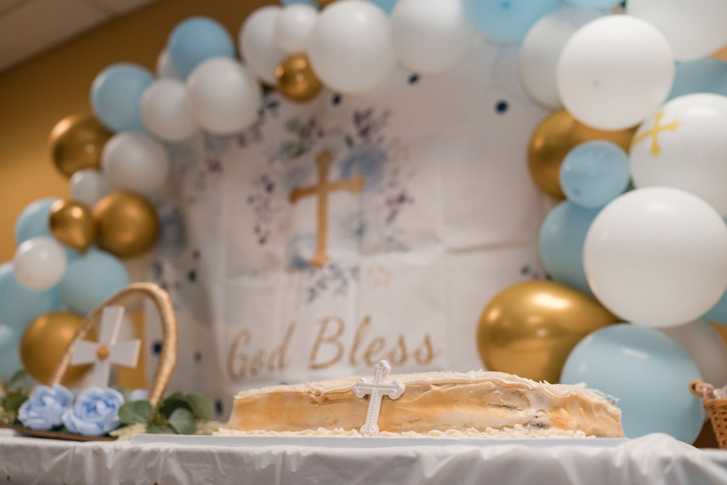 Baptism decoration featuring blue and gold balloon arch with 'God Bless' text and crosses.