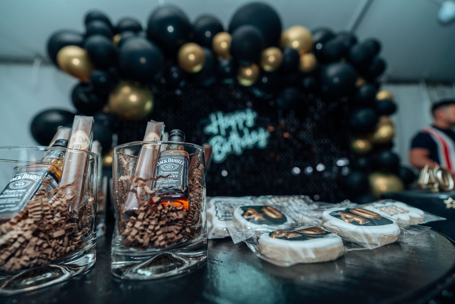 Elegant party setup with black and gold balloons, glass containers filled with treats, and decorative desserts.