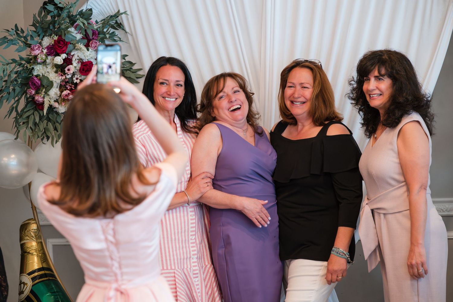 Group of women posing for photos at wedding celebration with floral decorations.