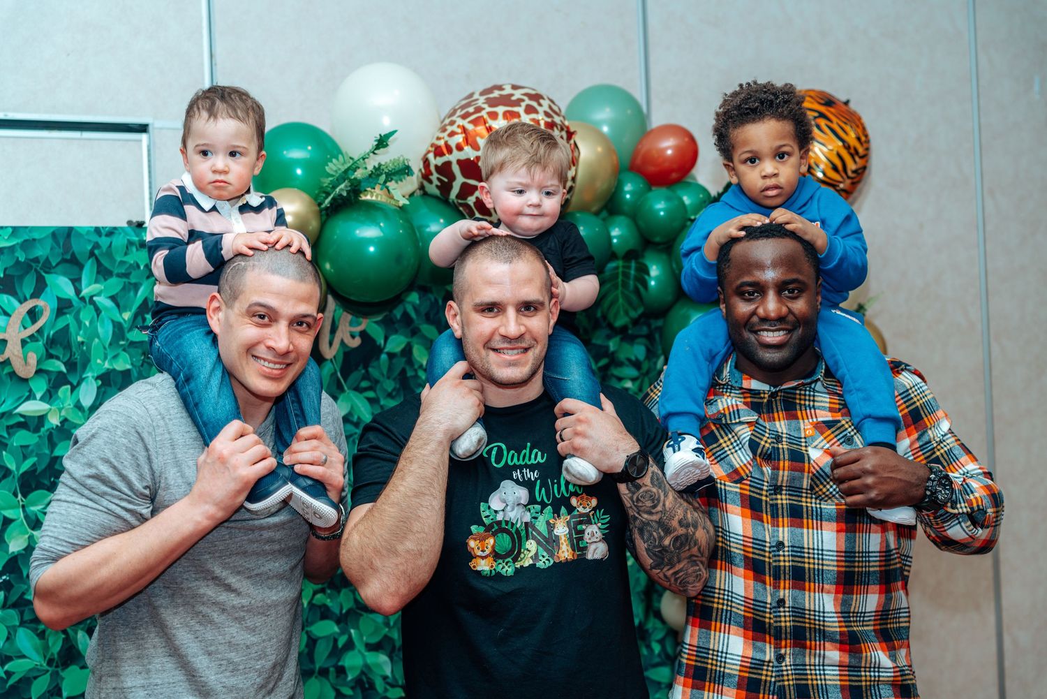 Group photo with children sitting on shoulders against balloon backdrop.