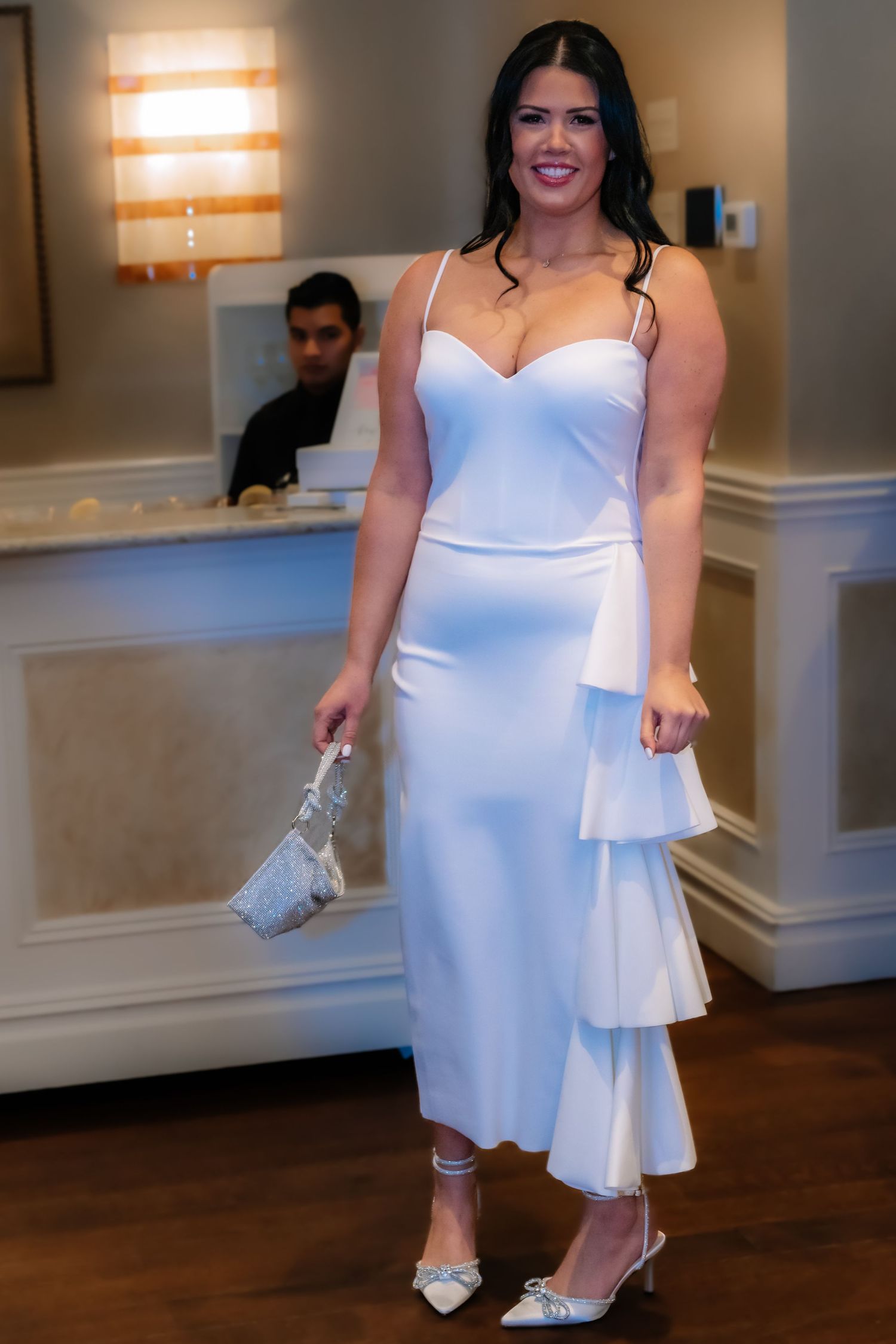 Woman in elegant white dress holding shoes at formal event.