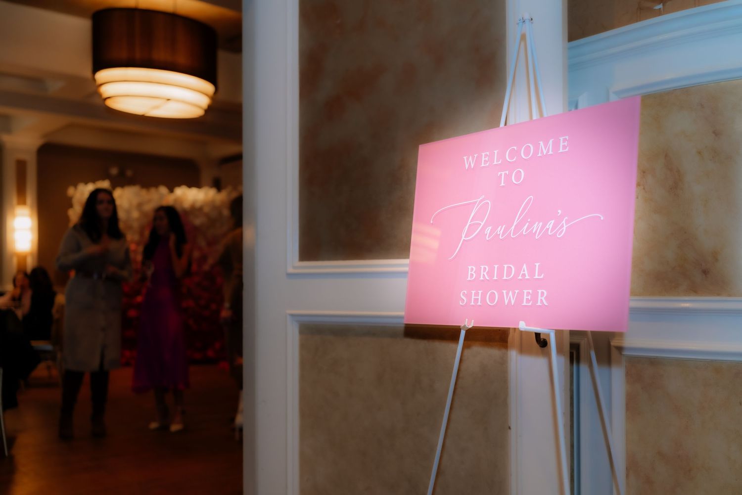 Pink welcome sign on easel at bridal shower or wedding event.
