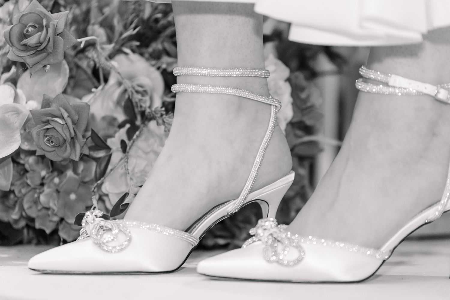 Elegant bridal shoes in white with delicate straps photographed in black and white.