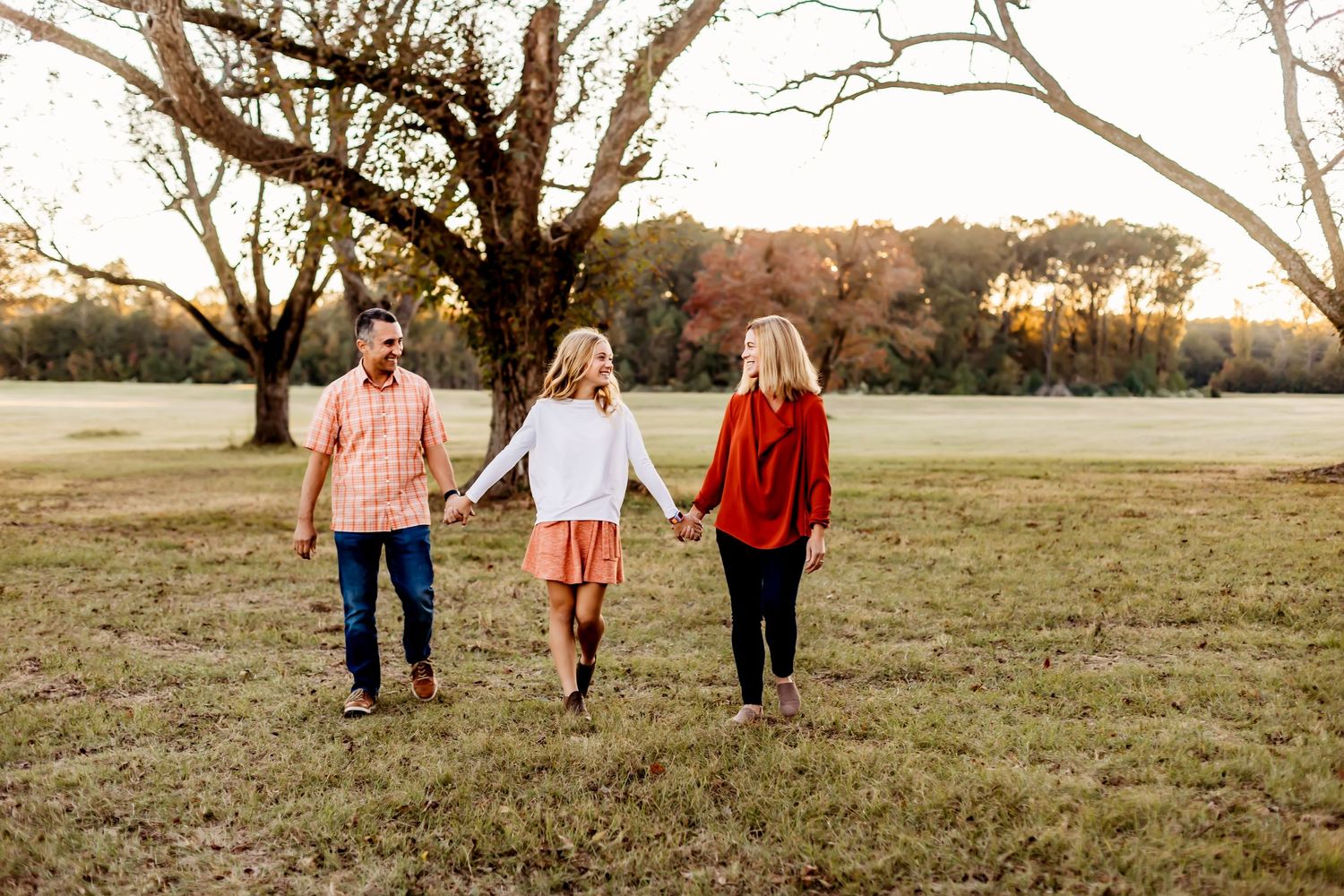 Three people walking hand in hand through a grassy field at golden hour.