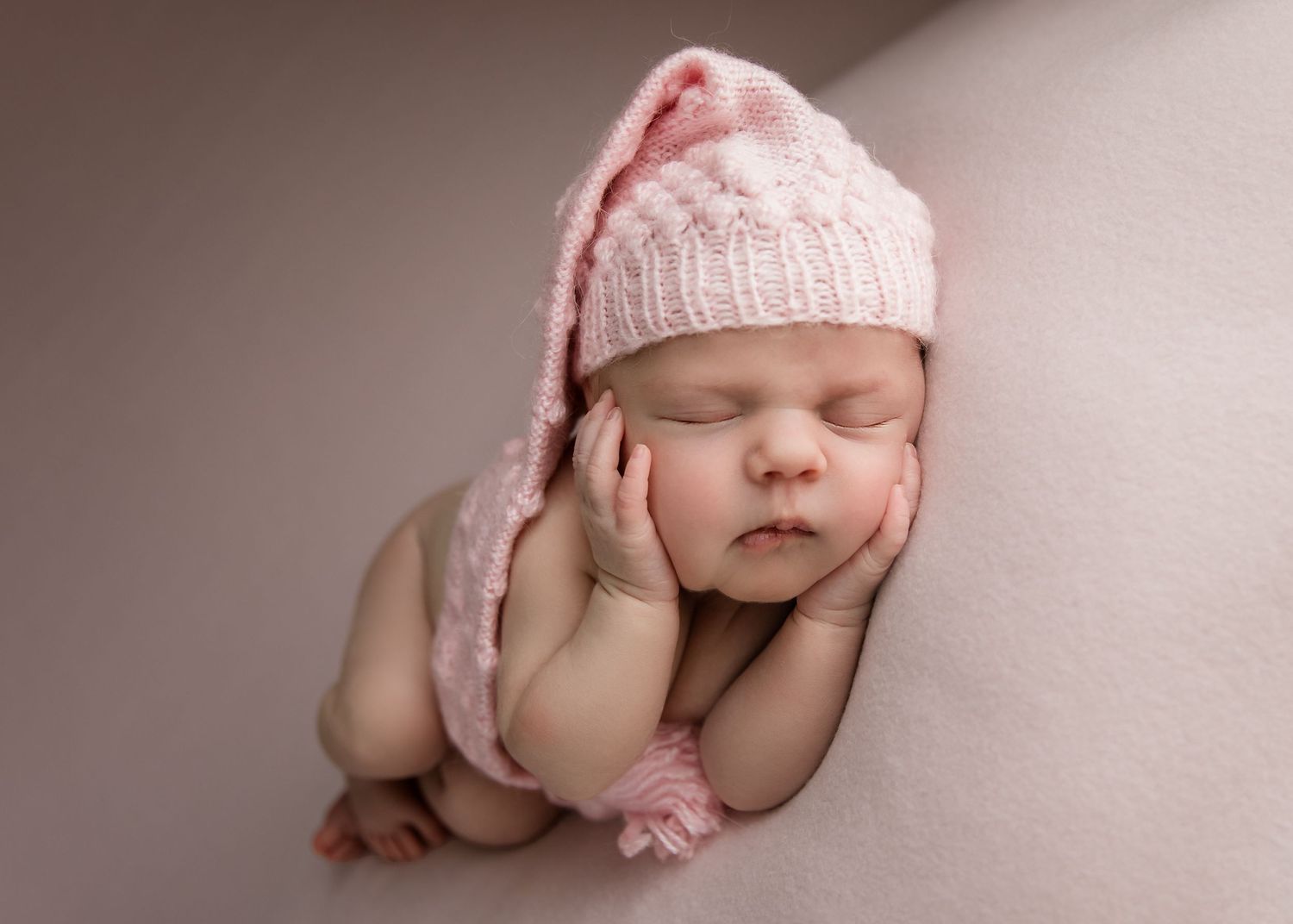 newborn baby in side pose with pink hat and backdrop