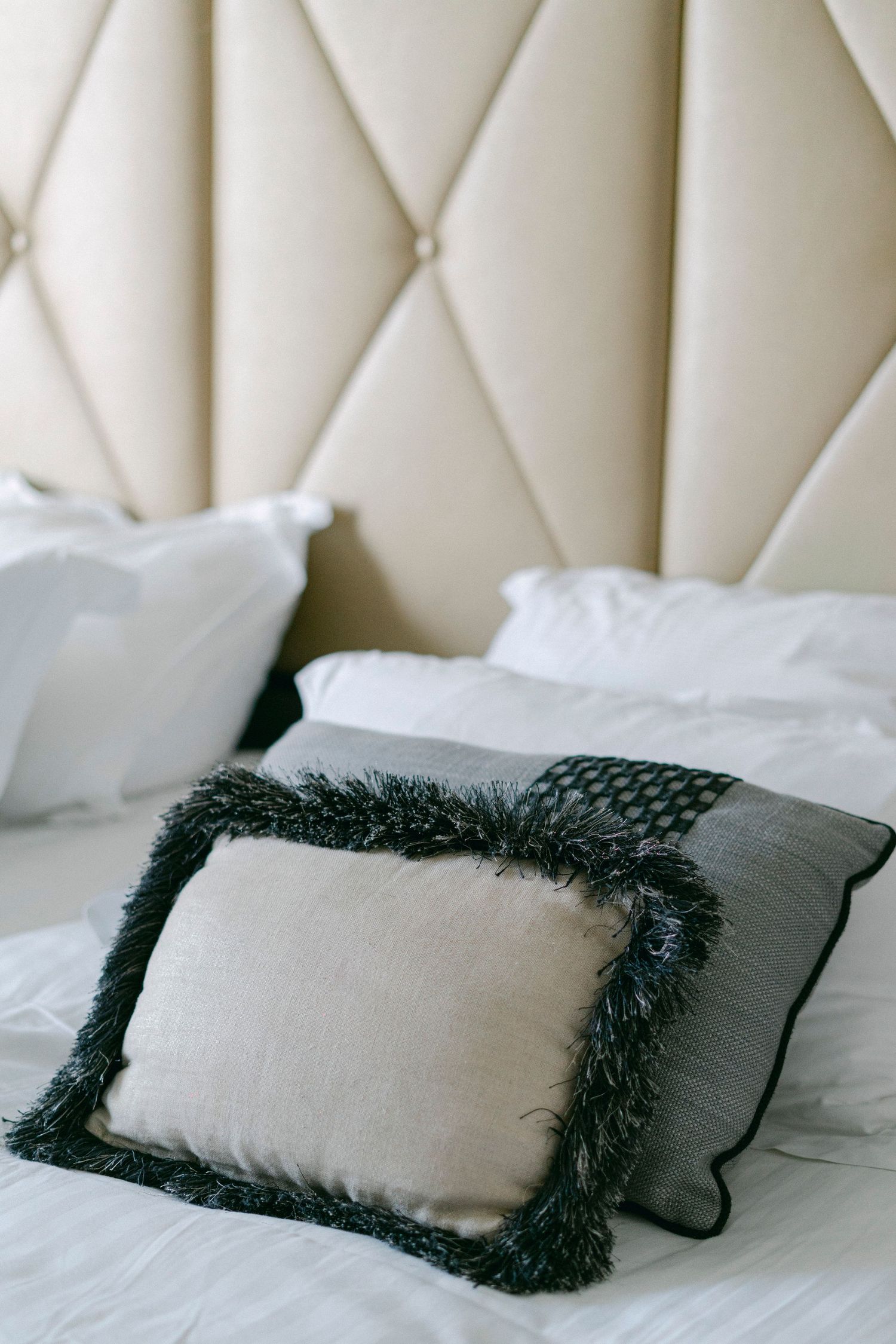 Luxurious tufted headboard with white bedding and decorative black-fringed pillow.