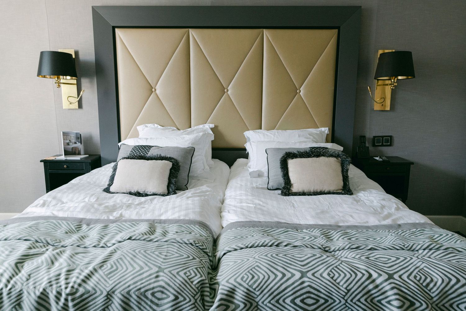 Modern hotel room with cream upholstered headboard and geometric patterned bedding.