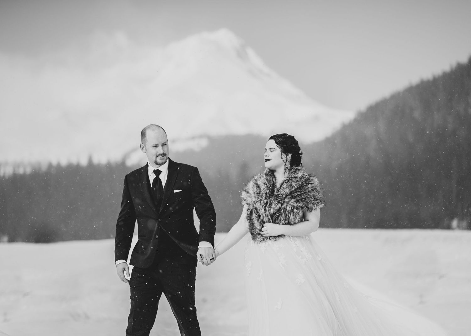 Black and white photo of a couple enjoying their winter wedding with a mountain backdrop.