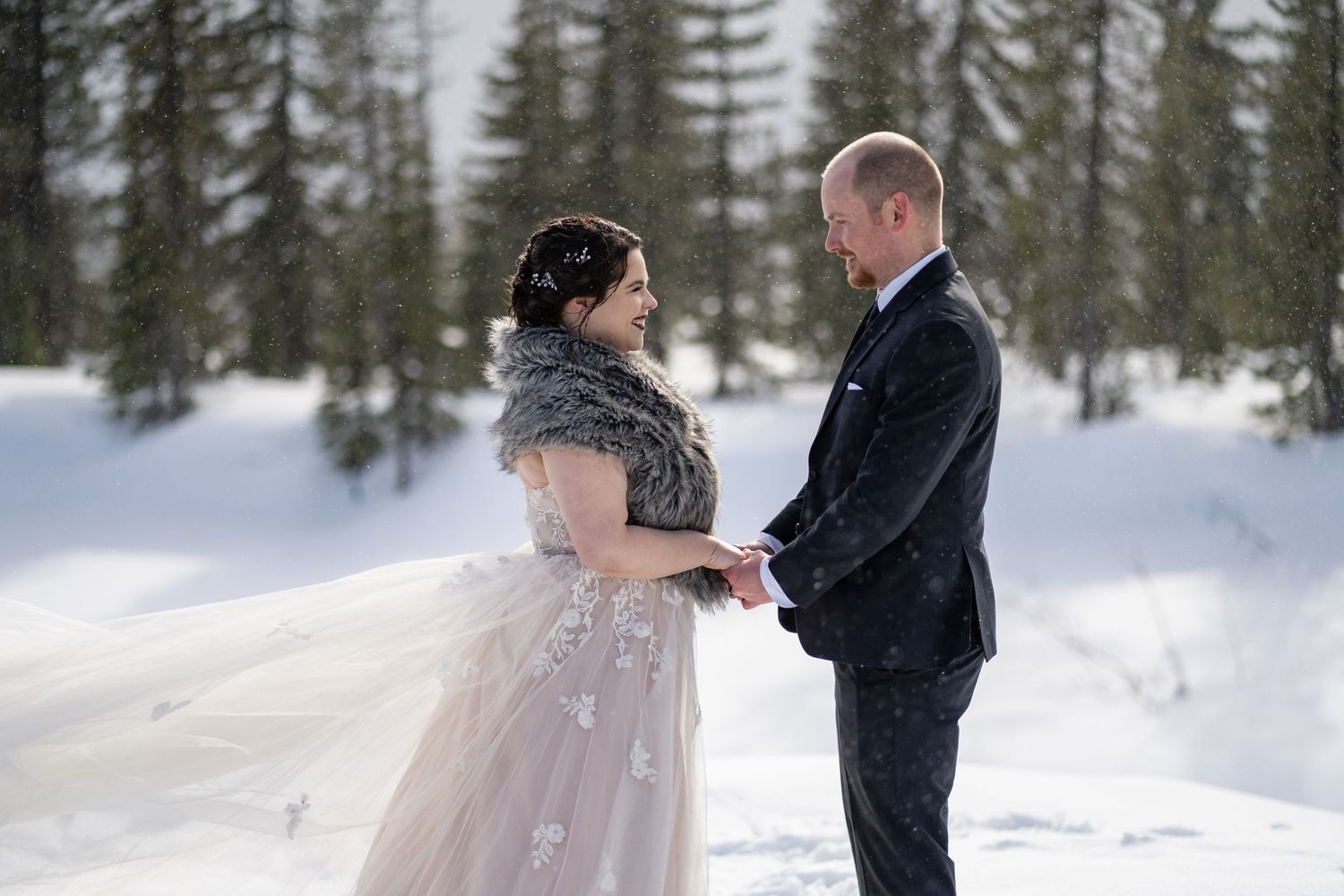 Winter wedding portrait with couple standing in snow surrounded by evergreen forest.