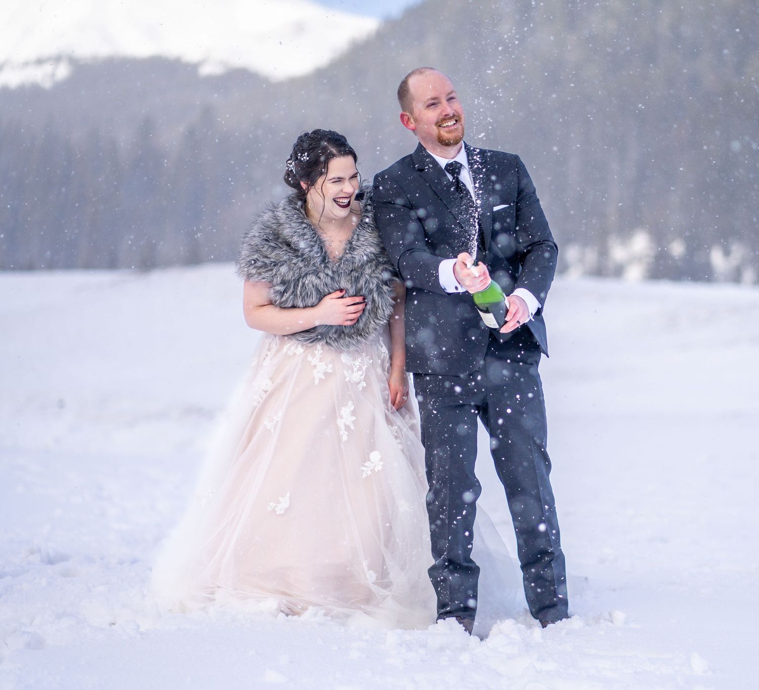 Couple celebrating their wedding in the snow with champagne and laughter.
