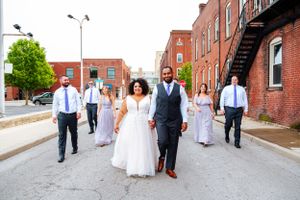 A wedding party walks down a brick-lined urban street together.