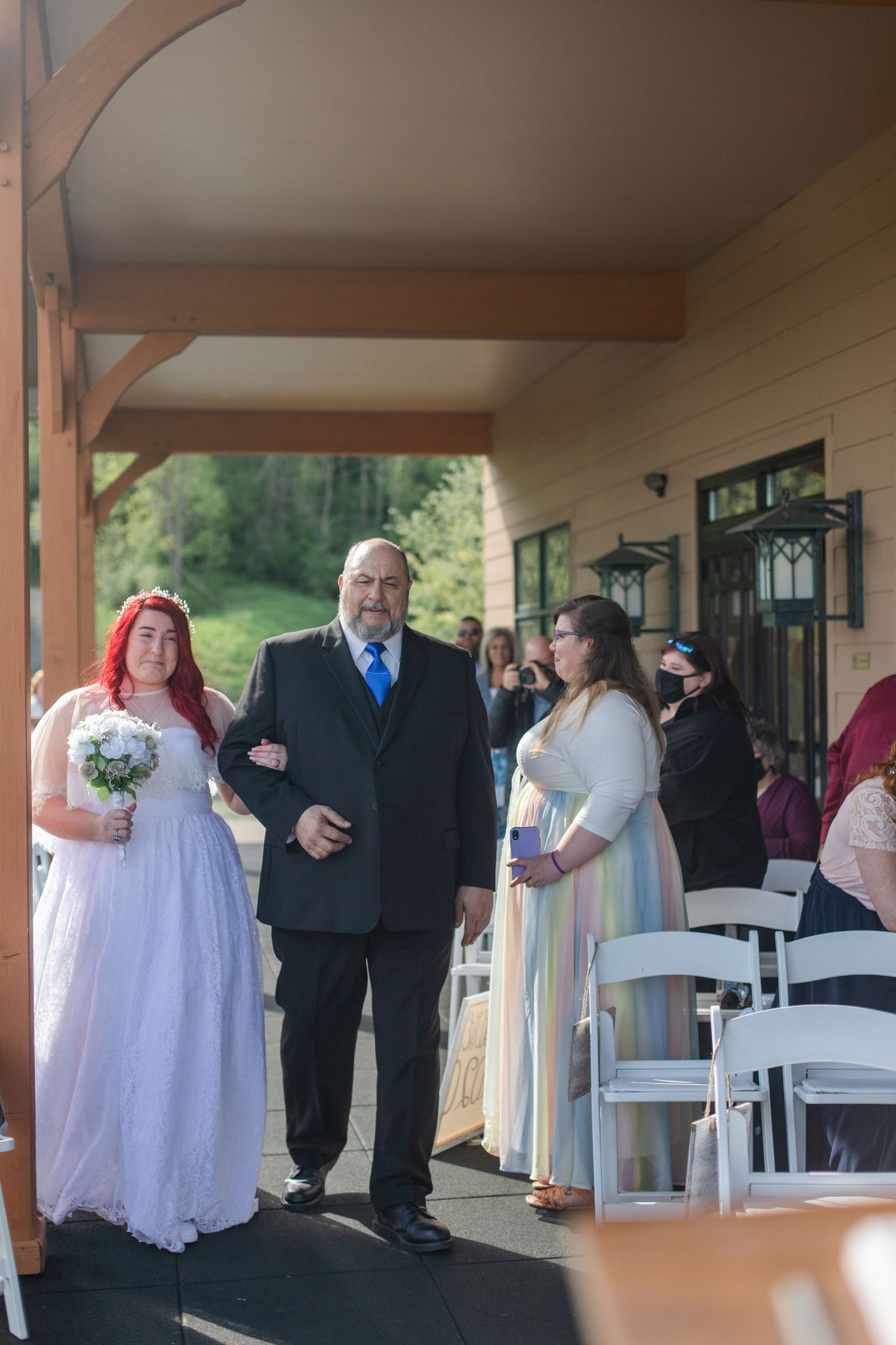 Wedding ceremony taking place on a covered outdoor patio with guests gathered around white chairs.