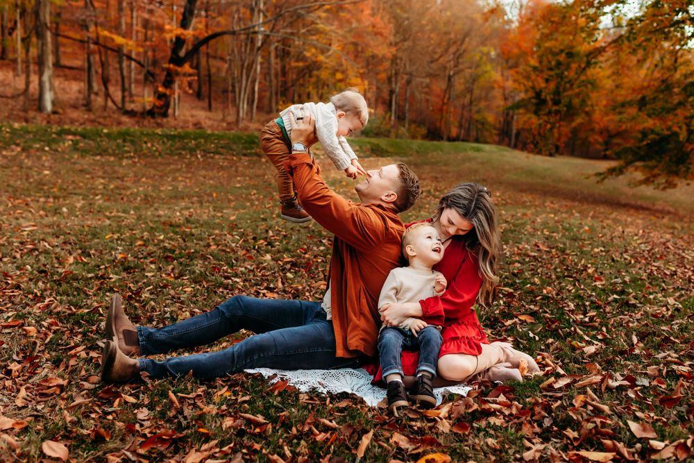 A young family plays together on a blanket surrounded by colorful fall foliage.