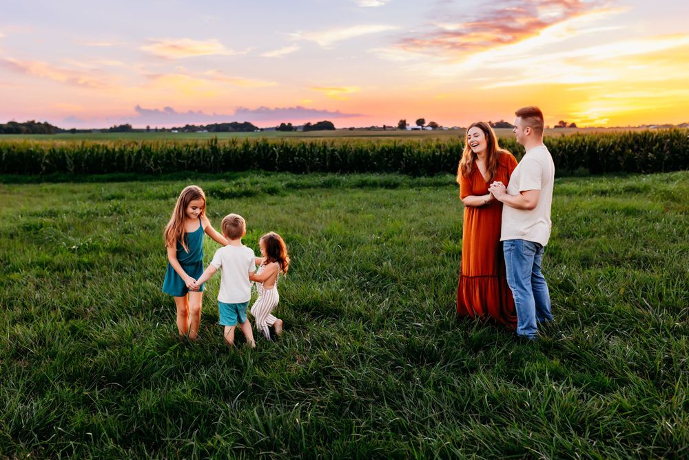 Family of five enjoying a beautiful sunset together in a green field near a cornfield.
