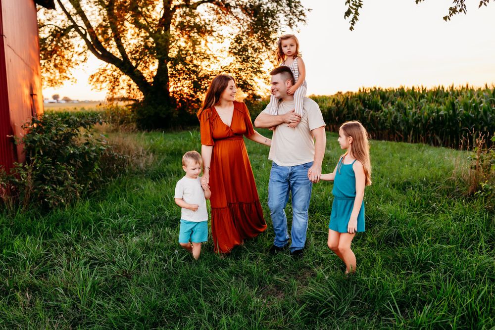 A family with three children enjoys a sunset stroll near a red barn in a green field.