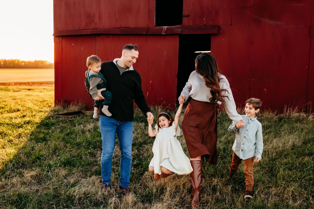 A family of five walks together near a red barn at golden hour sunset.